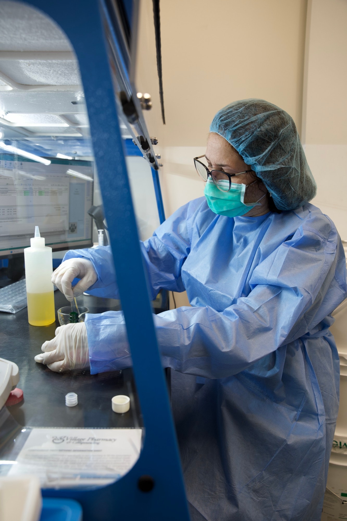 A Village pharmacist in full protective gear compounding a custom medication in the sterile lab